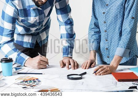 Man Carefully Studying Technical Drawing With Magnifying Glass. Designers Working With Color Swatche