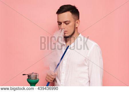 A Male Model Smokes A Hookah, Sheesha And Enjoys It. Pink Background