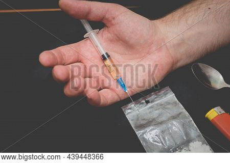 Drug Addict Hand With Syringe On Dark Room With A Bag Of Drugs A Spoon And A Lighter.toned.