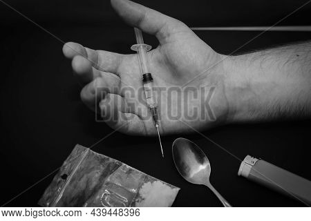 Drug Addict Hand With Syringe On Dark Room With A Bag Of Drugs A Spoon And A Lighter.toned.
