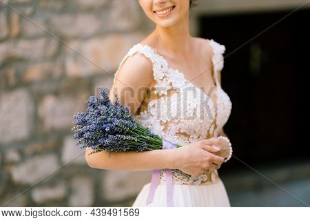 Sibenik, Croatia - 05.06.17: Smiling Bride In A White Lace Dress Holds A Lavender Bouquet On Her Elb