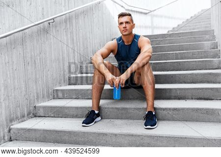 fitness, sport and people concept - tired young man with bottle of isotonic energy drink sitting on stairs