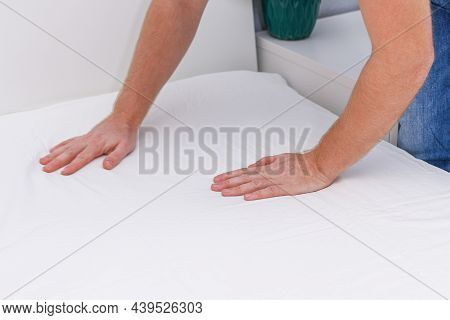 A Man Puts An Elasticated Sheet On The Mattress. Change Of Bed Linen.