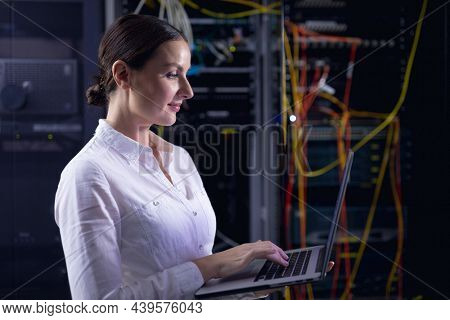 Caucasian female engineer using laptop in computer server room. database server management and maintenance concept