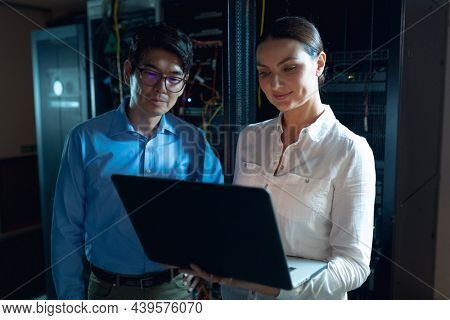 Diverse male and female engineers using laptop in computer server room. database server management and maintenance concept