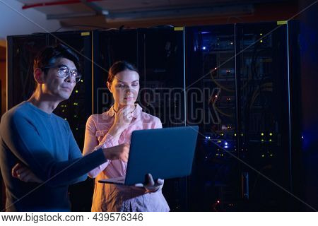 Diverse male and female engineers using laptop in computer server room. database server management and maintenance concept