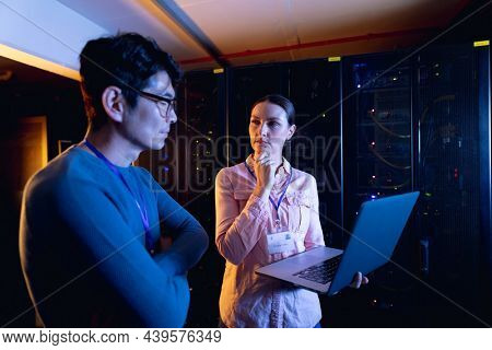 Diverse male and female engineers using laptop in computer server room. database server management and maintenance concept