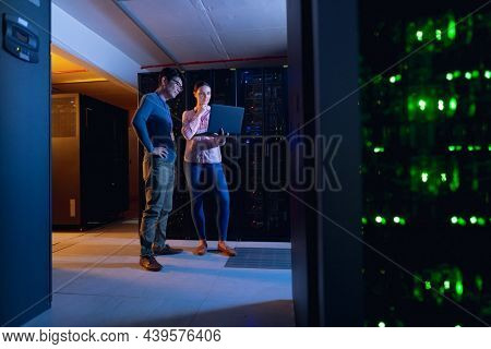 Diverse male and female engineers using laptop in computer server room. database server management and maintenance concept