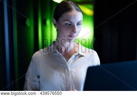 Caucasian female engineer using laptop in computer server room. database server management and maintenance concept