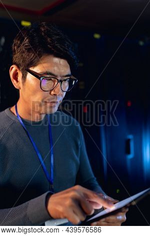 Asian male engineer using digital tablet in computer server room. database server management and maintenance concept