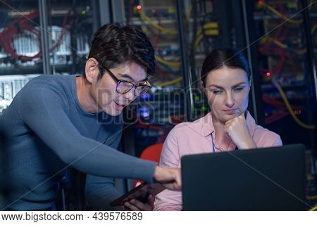 Diverse male and female engineers discussing over a laptop in computer server room. database server management and maintenance concept