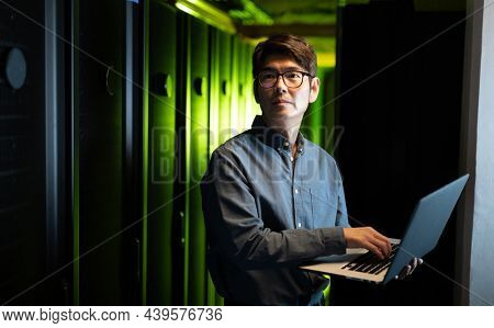 Asian male engineer using laptop in computer server room. database server management and maintenance concept