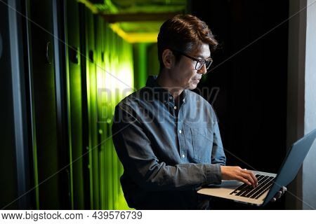 Asian male engineer using laptop in computer server room. database server management and maintenance concept