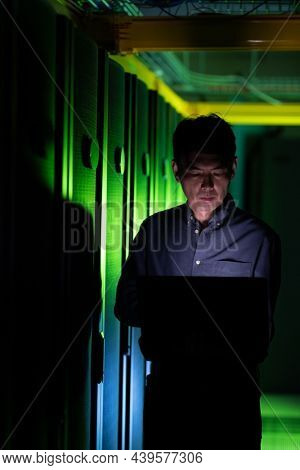 Asian male engineer using laptop in computer server room. database server management and maintenance concept