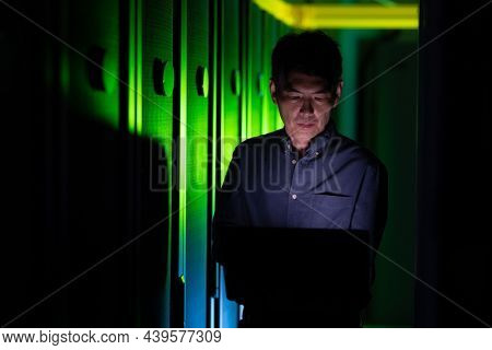 Asian male engineer using laptop in computer server room. database server management and maintenance concept
