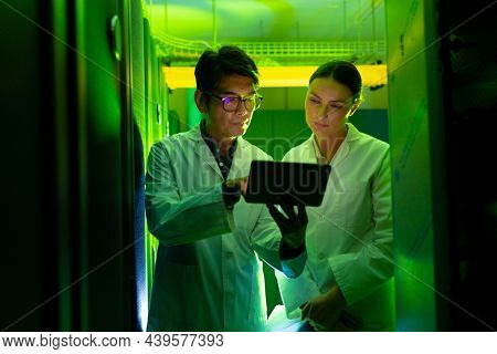Diverse male and female engineers wearing aprons using digital tablet in computer server room. database server management and maintenance concept