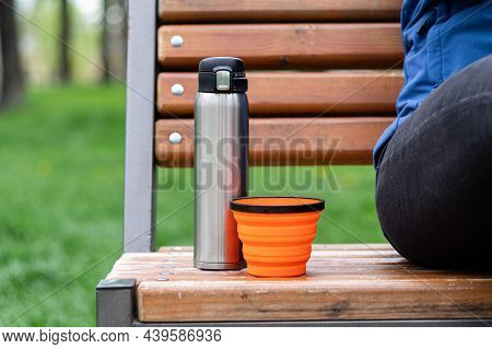 Steel Thermos And Silicone Mug. Tourist Dishes On The Bench. Drinking Coffee In The Park.