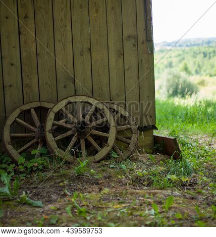 Vertical Photo Of Old Wooden Wagon Wheel Reclining On Wooden Wall. Wheel With Boardwalk Wall On Back