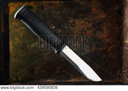 Knife With Black Plastic Handle. Shiny Stainless Blade. Knife On A Rusty Background. The Knife Is In