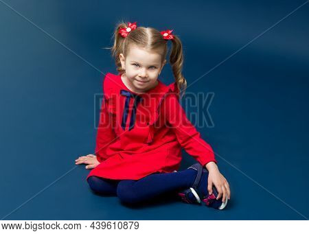 Cute Gray Eyed Girl In Red Dress Sitting On Floor. Adorable Little Girl With Cute Two Ponytails With