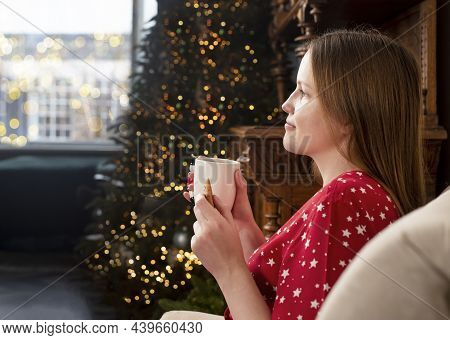 Woman With Tea Mug At Christmas Eve At Home. Person Relaxing Near Fir Tree And Windiw With Lights On