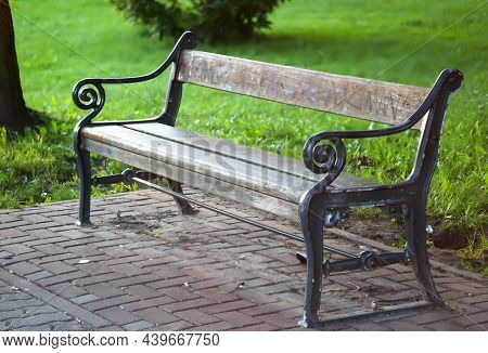 A Cast Iron Park Bench Stands At The Edge Of A Path In A Park.