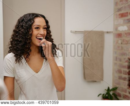 Mirror Reflection Of A Young African American Woman Smiling Whilst Brushing Her Teeth In The Bathroo