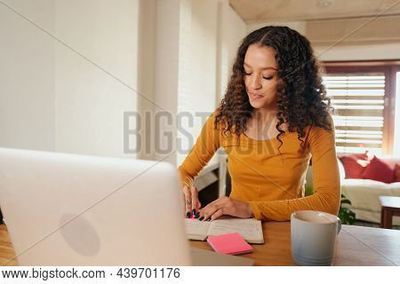 Multi-cultural Female Making Notes In Notebook. Young Professional Remote Working With Laptop In Mod