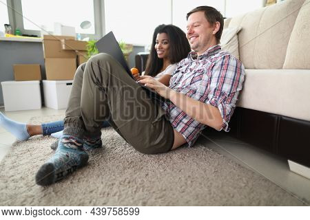 Low Angle Of Cheerful Smiling Couple Watch Show Online On Laptop At Home. Man And Latin Girl Sit On 