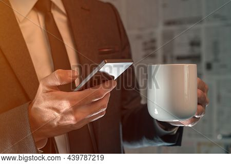 Businessman Drinking Coffee And Using Mobile Phone In Fake News Infodemic Concept With Tabloid Newsp