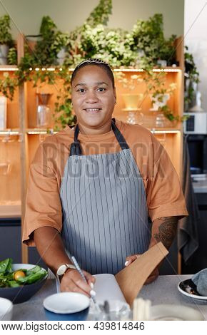 Vertical Medium Portrait Of Young Adult Black Woman Working In Small Cafe Kitchen Writing Down List 