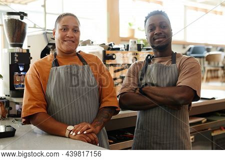 Horizontal Medium Portrait Of Modern Young Co-workers Wearing Aprons Standing At Cafe Counter Agains