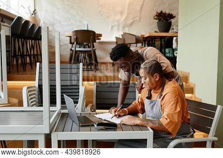 Young Man And Woman Working Together In Modern Cafe Starting Workday Checking List Of Products For D