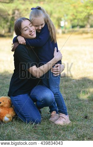 Two Sisters, The Youngest And The Oldest, Hug In The Park During The Warm Season. There Is A Teddy B