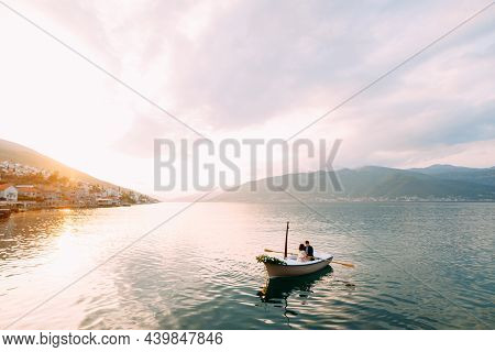 Man Rolls Woman In A Boat With Flowers On The Water On The Mountains And Sunset