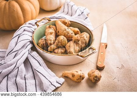 Raw topinambour with pumpkins in bowl on kitchen table