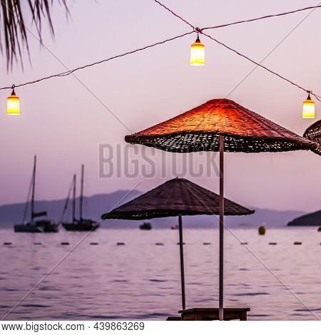 Beach Umbrellas And Lanterns Against The Backdrop Of The Sea, Islands And Yachts At Sunset. Summer V