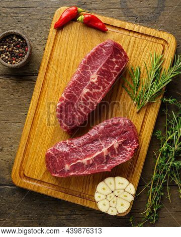 Vertical Of Two Raw Top Blade Beef Steak On Wood Board With And Herbs