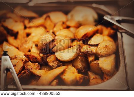 A Lot Of Delicious Appetizing Fried Rustic Potatoes Are In The Fryer, Next To Which There Are Tongs.