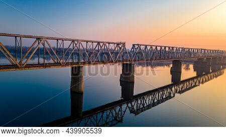 Aerial View Of The Railway Bridge, Which Is Reflected Over The Calm River Dnieper Before Dawn In The