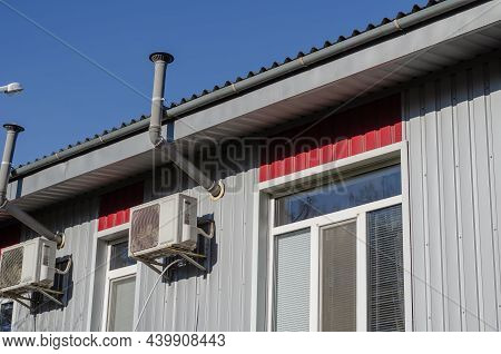 A Gray-red Industrial Building Against A Blue Sky. The Building Is Lined With Metal Profile Sheets. 