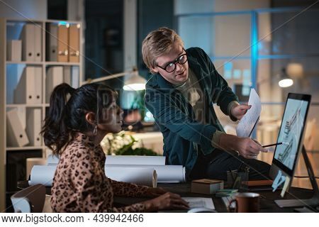 Young Designer Pointing At Computer Monitor And Discussing Blueprint With His Colleague During Their
