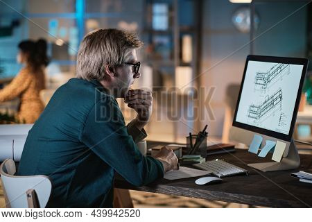 Young Designer In Eyeglasses Sitting At The Table And Looking At Computer Monitor, He Developing New