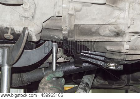 Mechanic In Work Gloves Using A Wrench Unscrew The Transmission Of The Car From The Body Of The Inte