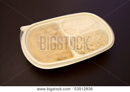 Closed package wit frozen food - Chicken stroganoff with rice and shoestring potatoes - Package on brown leather background.