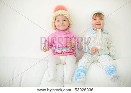  Two little kids in hats sit on back of white sofa at home. Shallow depth of field.
