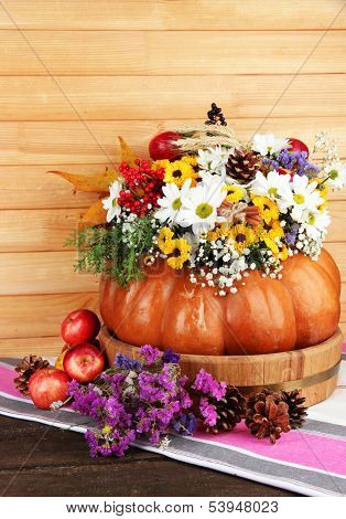 Beautiful autumn composition in pumpkin with apples and bumps on table on wooden background