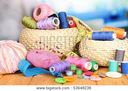 Wicker baskets with accessories for needlework on wooden table, on bright background