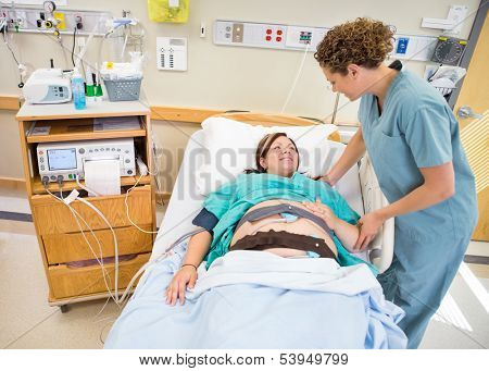 Mid adult female nurse communicating with pregnant patient lying in hospital bed