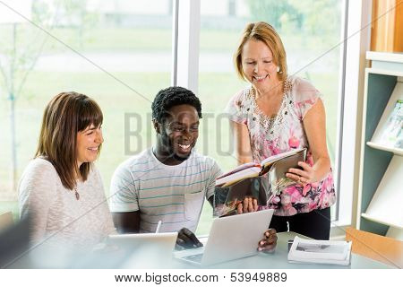 Happy mature librarian assisting university students in library